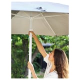 A woman adjusts a beige HÖGÖN parasol in an outdoor setting, ensuring shade.