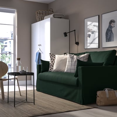 Modern living room with green HYLTARP sofa, large art, sleek table, cozy rug, and white storage unit.