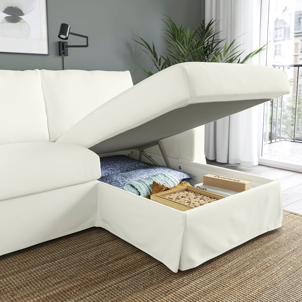 A modern white sofa with a lift-up chaise longue revealing board games and blankets in storage.