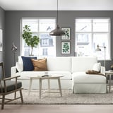 Modern living room with white sofa, dark wall, large windows, hanging lamp, round coffee table, grey chair with beige cushion.