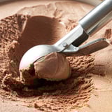 Metal ice cream scoop holding chocolate ice cream, with a lever to release scoop easily.