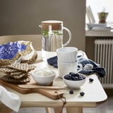 Rustic table setting with stackable mugs, bowls, blueberries, yogurt, water, mint, and waffles.