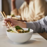 Person holding chopsticks over a bowl of vegetable soup on a table.