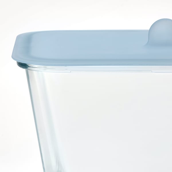 Close-up of a clear glass container with a blue silicone lid, designed for food storage and oven use. The lid a lip for easy handling.
