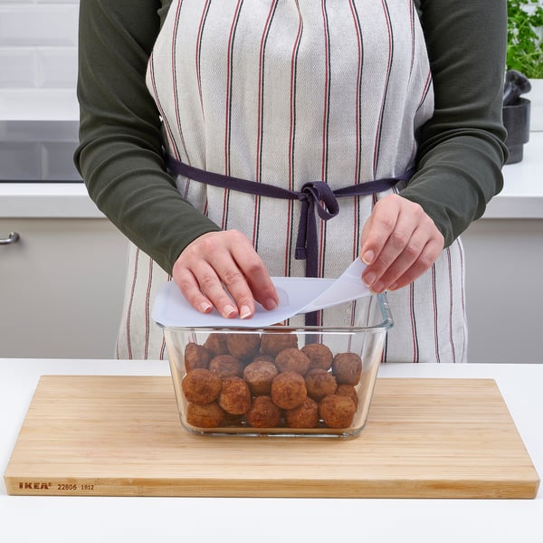 Person placing a glass container with food on a wooden board. The container has a vacuum-creating lid.