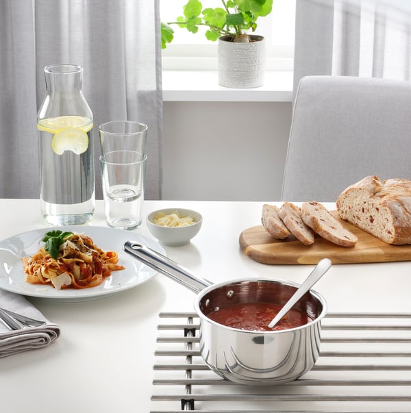 A kitchen setup with a saucepan of sauce, bread slices, and a carafe on a table.