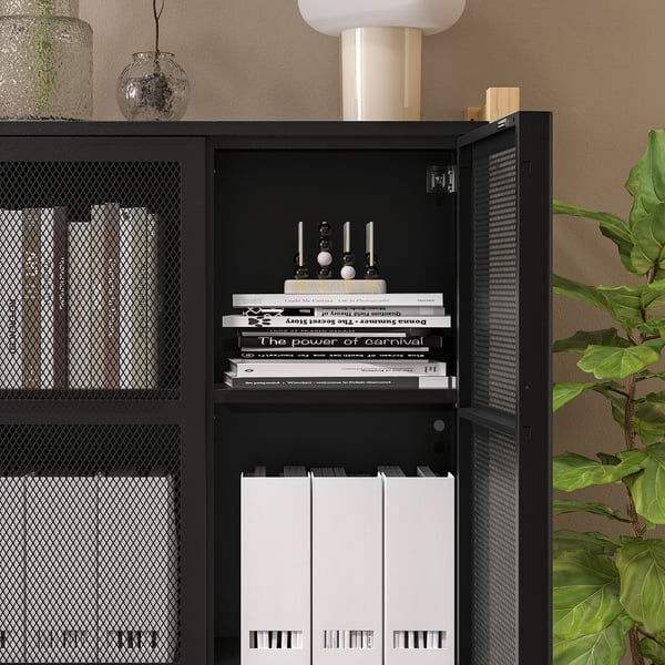 Black IVAR storage unit with mesh doors, holding books and vinyl records, placed against a wall.