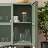Green IVAR storage unit with glass doors displaying kitchen items.