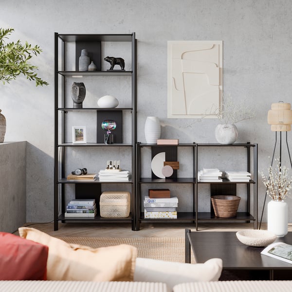 Modern living space with glass bookshelves, containing vases, books, and decor, against a grey wall with abstract art and a red sofa.