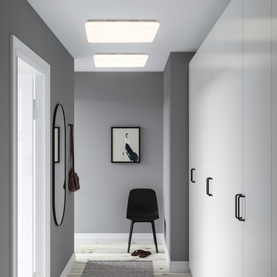 Modern hallway with grey walls, slim light panel, black chair, shoe rack, round mirror, and small rug.