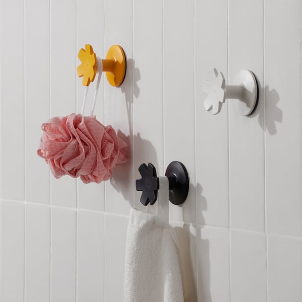 Three colorful snowflake hooks hang items in a bathroom. One holds a pink loofah, another a white towel. Easy-to-attach, practical storage.