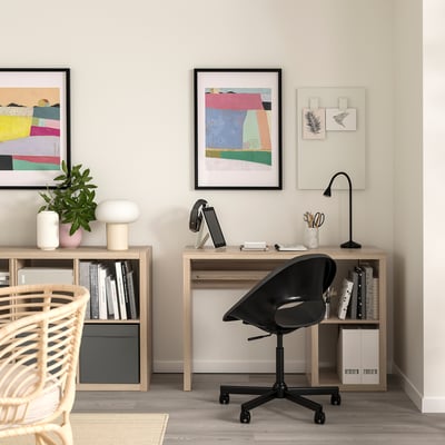 Home office with wooden desk, black swivel chair, and bookshelves, adorned with colorful art and neat decor.