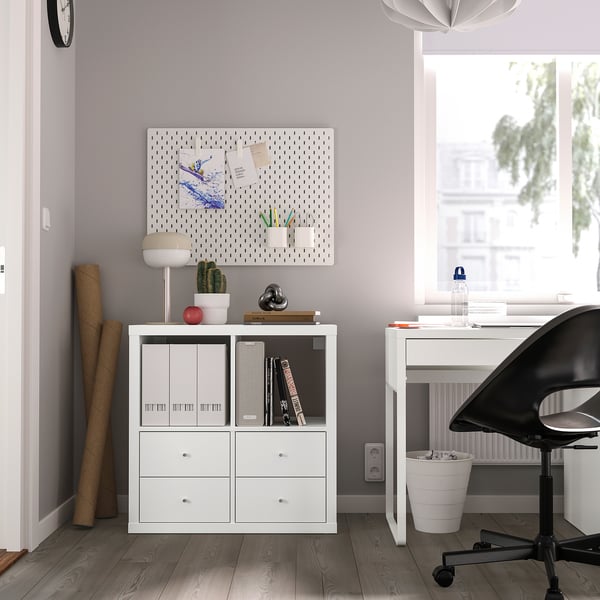 Minimalist home office with KALLAX unit, notes, cactus, lamp, and pegboard art. Black chair at desk by window.