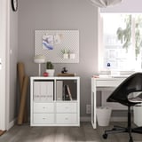 Minimalist home office with KALLAX unit, notes, cactus, lamp, and pegboard art. Black chair at desk by window.