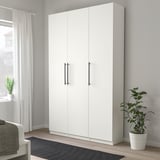 Large white KALLRÖR wardrobe with black handles stands tall next to gray wall, near window and potted plant.