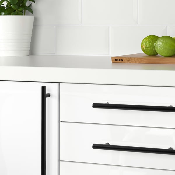 White kitchen cabinets with black handles; green potted plant and limes on counter.