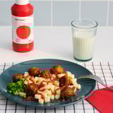 A meal with peas, potatoes, sausage, KETCHUP, milk, on a checkered tablecloth.