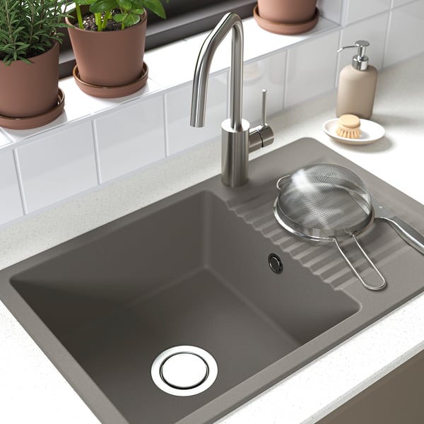 Black sink with stainless faucet and strainer; plants nearby.