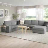 Modern living room with large gray KIVIK sectional sofa, two side tables, rug, and large window with view of greenery.