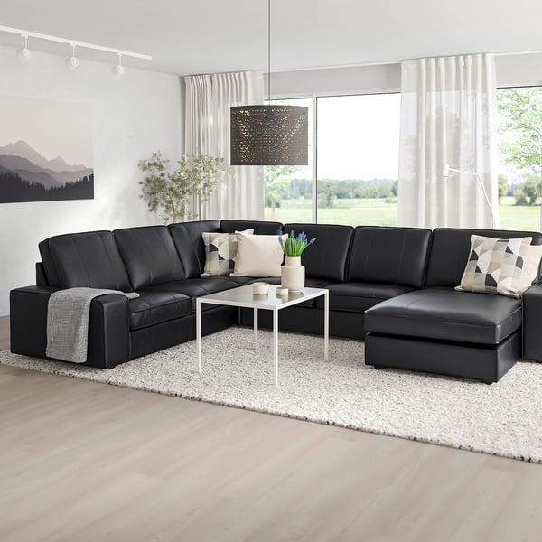Elton black KIVIK sectional, leather & fabric blend, large & comfy, wide armrests, positioned before tall windows, complemented by white decor.