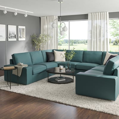 Modern living room with large teal KIVIK sectional sofa, black coffee table, white rug, and large windows with curtains.