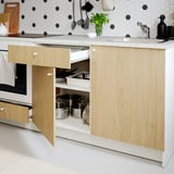 Modern kitchen with wood cabinet, open drawer, pans, marble countertop, and sink.