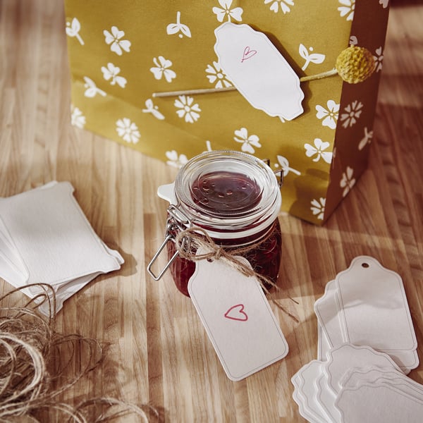 Jar with dark contents beside yellow gift bag, heart tag, jute, on wood.