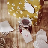 Jar with dark contents beside yellow gift bag, heart tag, jute, on wood.