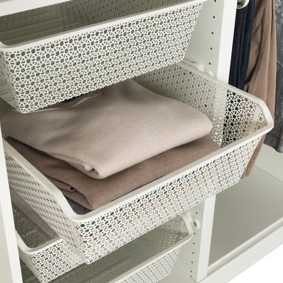White metal baskets in wardrobe storing folded clothes, allowing air circulation.