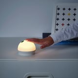 A hand turns on the KORNSNÖ touch nightlight on a drawer, revealing its soft glow.