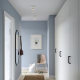 A modern hallway a white ceiling track with 2 adjustable spots, almost invisible, beside a large mirror and hooks.
