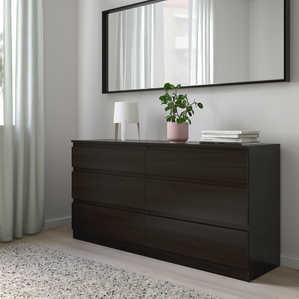 Dark brown dresser with mirror and drawers. Lamp, books, plant on top. Rug, safe, anchored.