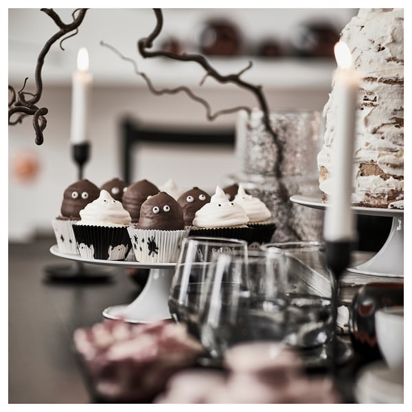 Ghostly cupcakes in KUSTFYR black & white cups sit on a cake stand, smaller than wine glasses nearby. Branches and candles decorate the table.