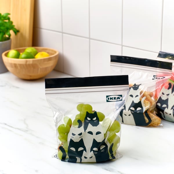 Two sealed bags with cat designs hold grapes and snacks. One bag is labeled ikea.