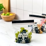 Two sealed bags with cat designs hold grapes and snacks. One bag is labeled ikea.