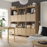 Light wood storage unit with open/closed shelves, holding decor, books, office supplies against dark wall.