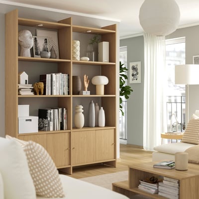 Wooden storage unit with open and closed shelves, white decor items, lamp, and windows. Modern minimalist living room.