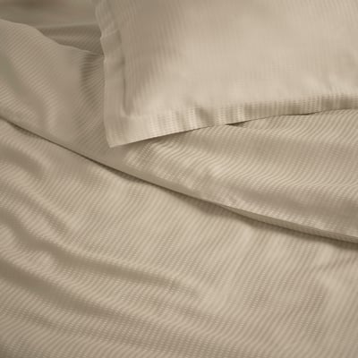 Folded beige bedding set. Includes duvet cover and pillows with flanged trim. Soft, silky lyocell fabric.