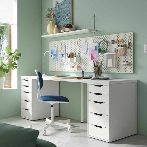 Home office setup with white LAGKAPTEN desk, blue chair, drawing supplies, and pegboard. Desk is large, fitting extra seating.
