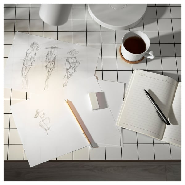 Creative workspace: white sketches, open notebook, pen, cup, on black grid table.