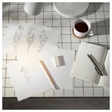Creative workspace: white sketches, open notebook, pen, cup, on black grid table.