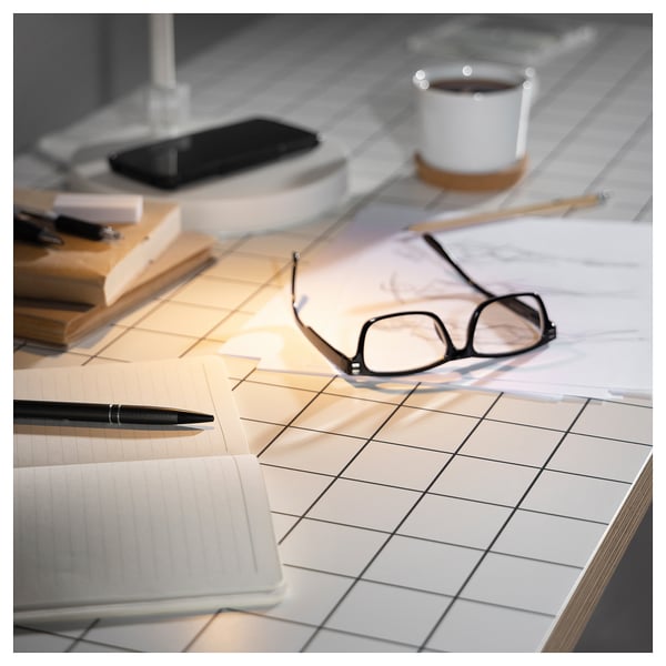 Desk with white grid tabletop, black glasses, pen, and coffee mug. Minimalist and organized workspace.