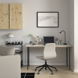 Modern home office with white LAGKAPTEN desk, gray chair, computer, headphones, and lamp against a gray wall with wooden panel and map.