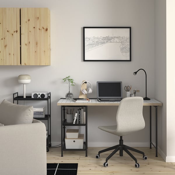 Minimalist home office with LAGKAPTEN desk, monitor, plant, headphones, lamp, cityscape print, sofa, bookshelf, and gray chair.