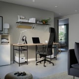 Modern home office with desk, chair, laptop, lamp, headphones, books, plants, cabinet, sofa.