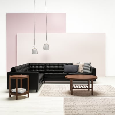 Modern living room with black l-shaped sofa, wooden tables, and pink accents. Two pendant lights hang above.