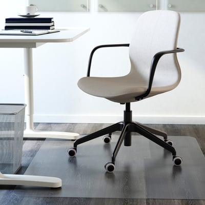 Modern office chair with lumbar support and adjustable height, on transparent mat, beside white desk with books.