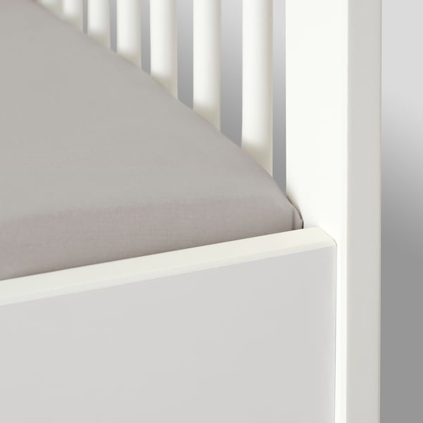 A white crib with a gray fitted sheet, secured by elastic for a tight fit.