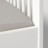 A white crib with a gray fitted sheet, secured by elastic for a tight fit.
