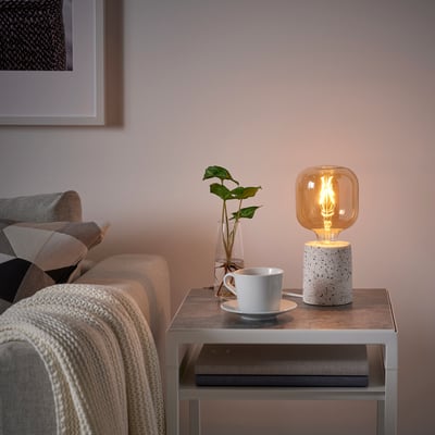 Cozy living room corner with LERSKIFFER lamp, coffee, plant, and blanket sofa.